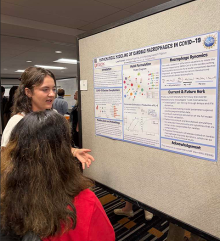 Lisa Kranec presenting her research with her poster to another person with long brown hair. 